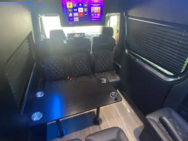 Executive Sprinter cabin with a TV at the front, blue skylight and leather seats by a dark table — Shuttle Service New Jersey — Mercedes Sprinter