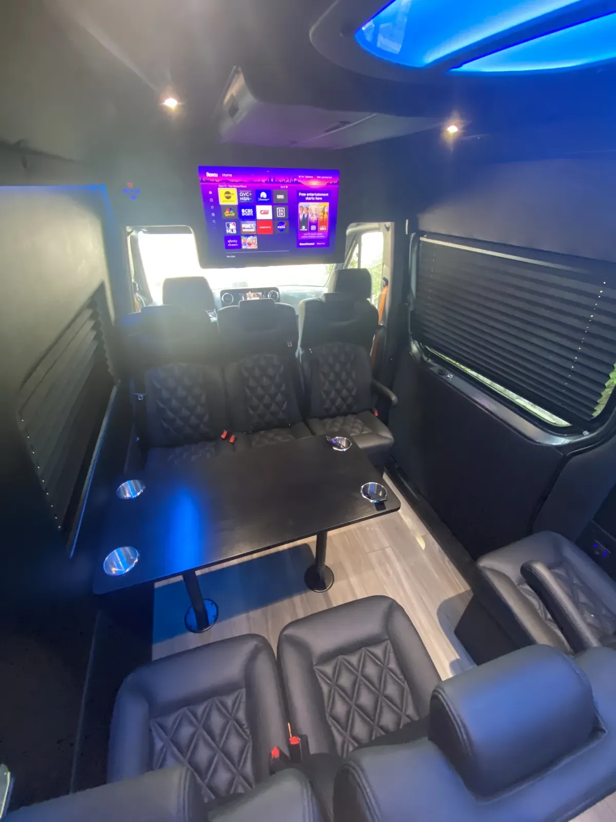 Executive Sprinter cabin with a TV at the front, blue skylight and leather seats by a dark table — Private Transfer NYC