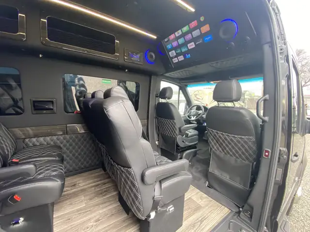 Executive Sprinter cabin through the side door, showing leather captain seats and a ceiling entertainment panel — Shuttle Service Long Island — Mercedes Sprinter