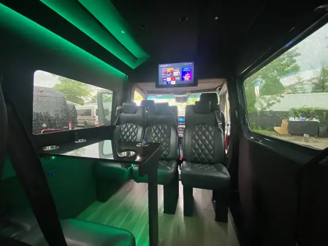 Executive Sprinter with green ceiling lighting, a front TV and leather seats around a glass table — Corporate Transportation New Jersey — Mercedes Sprinter