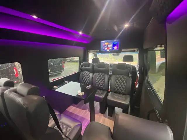 Executive Sprinter with purple ceiling lighting, a ceiling TV and black leather seats around a table — Sprinter service in Tribeca