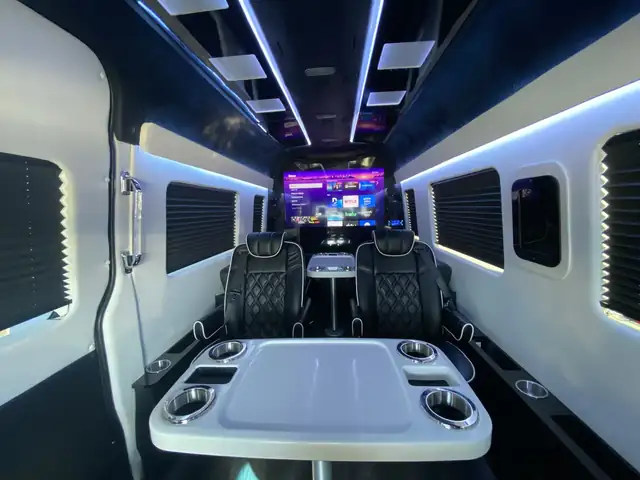 Jet Sprinter with black captain chairs, a white conference table with cup holders and a TV ahead — Private Transfer NYC