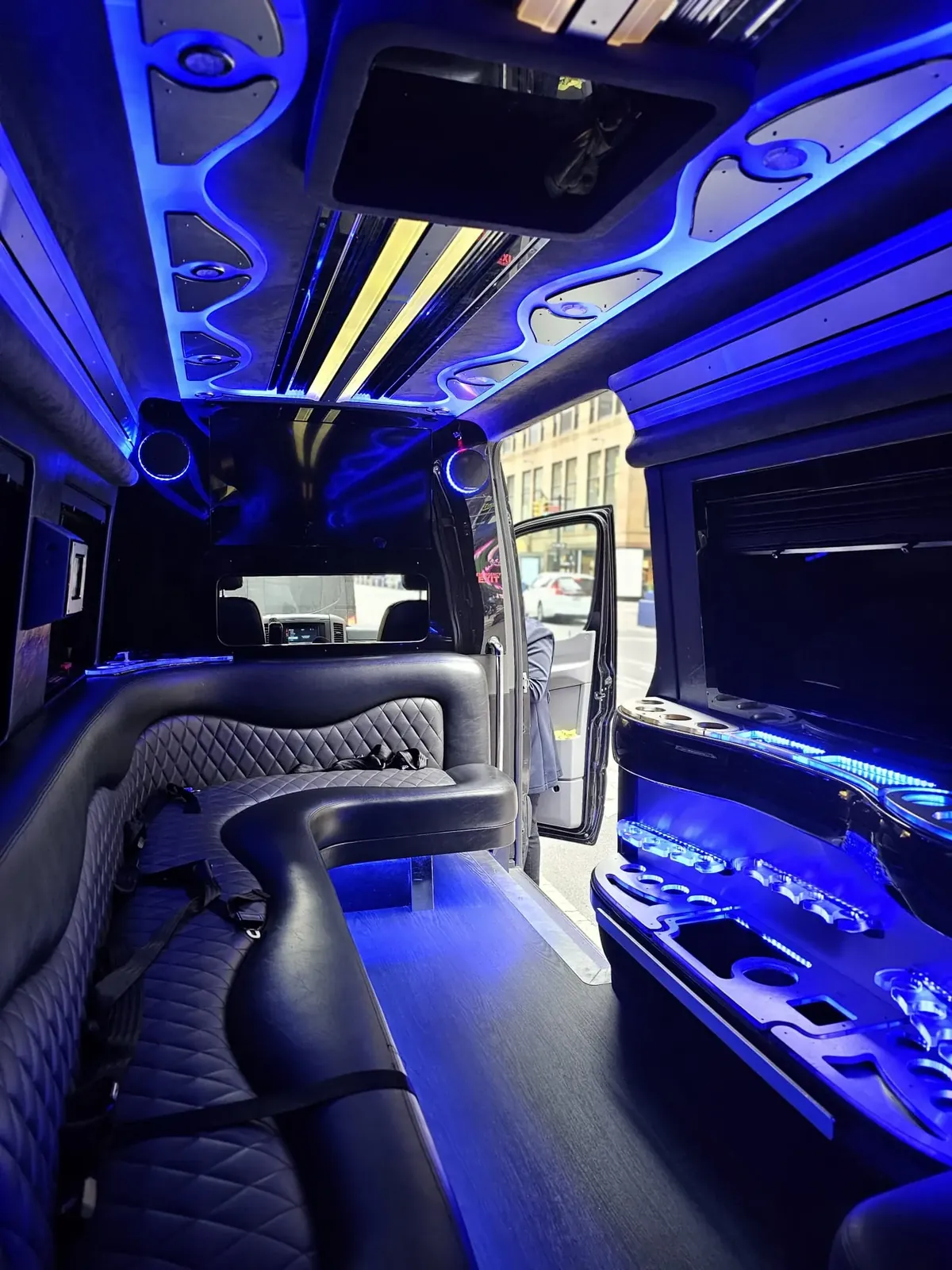 Limo Sprinter with a curved black sofa, blue light strips and a side door open to the street — Wedding Shuttle Service New Jersey — Mercedes Sprinter
